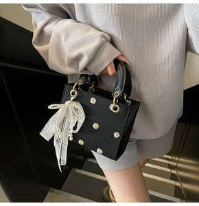 Detail of black daisy print handbag featuring pearl lace bow charm and gold hardware