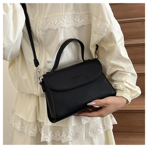 Gros plan d'un sac à bandoulière en cuir grainé noir porté par un mannequin en dentelle