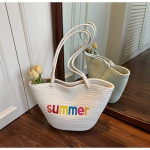 Detail of cream woven tote bag featuring colorful summer embroidery and long handles