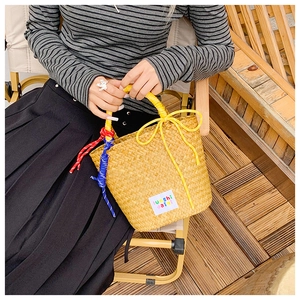 Detail of yellow woven straw bucket bag featuring a bow and decorative colorful ropes