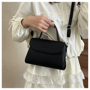 Gros plan d'un sac bandoulière noir grainé porté par un mannequin en robe de dentelle