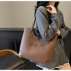 Macro detail of the brown leather tote bag showing embossed WWTU lettering and gold rivets