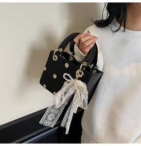 Close-up of black crossbody bag with daisy embroidery and lace pearl bow charm