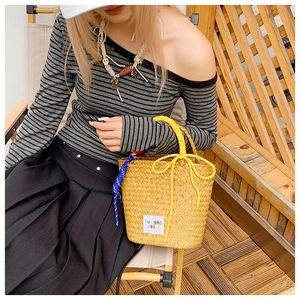Detail of woven straw bucket bag with yellow handles and bow on summer striped dress