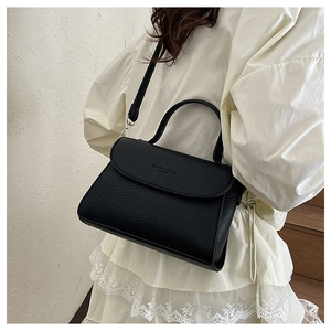 Détail d'un sac bandoulière noir à motif litchi avec poignée supérieure et cuir texturé