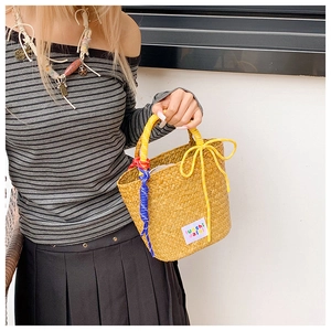 Detail of woven straw handbag with yellow handle and decorative colored tassels
