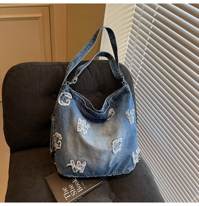 Detail of vintage denim tote bag showing white frayed letter patches and washed fabric