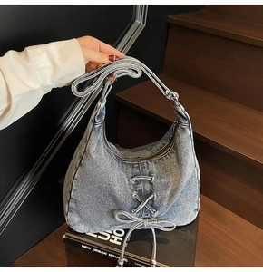 Détail du sac bandoulière en jean bleu avec nœud décoratif sur un livre noir