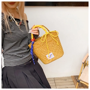 Close-up of woven straw bucket bag featuring yellow bow detail and vibrant colorful brand tag