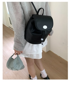 Detail of black pebbled leather backpack with silver round buckle and drawstring closure
