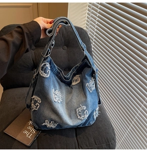 Detail of blue denim hobo bag featuring distressed G letter patches and adjustable strap