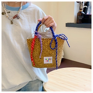 Detailed shot of handmade straw beach bag with vibrant colorful braided handles and drawstring