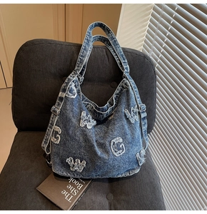 Detailed macro of vintage denim tote bag with frayed letter patches on a velvet chair