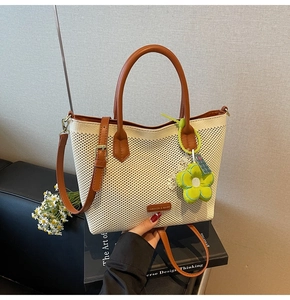 Détail du cabas en maille tressée avec poignées en cuir marron et pendentif fleur verte