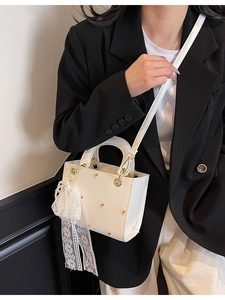 White crossbody bag with daisy embroidery and pearl lace charm on model with black suit