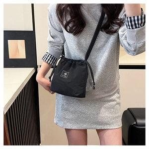 Close-up of black nylon drawstring bucket bag with AILANZI logo tag on grey outfit