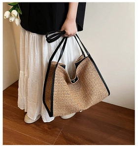 Spacious woven straw tote bag with black leather handles shown on shoulder for beach or commute