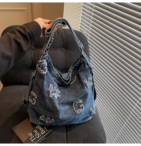 Detail of blue denim hobo bag featuring vintage frayed letter patch and wide shoulder strap