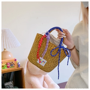 Detail of woven straw tote bag featuring colorful braided rope handles and tassel accents