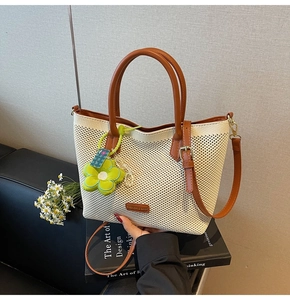 Détail du sac cabas tissé crème avec poignées en cuir marron et pendentif fleur verte