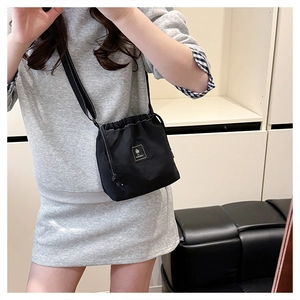 Detail of black drawstring crossbody bucket bag with adjustable strap and logo label