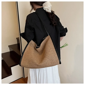 Close-up of brown herringbone woven straw tote bag with black leather shoulder straps
