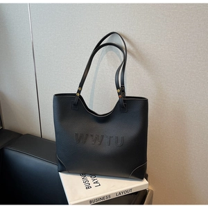 Close-up of black leather tote bag featuring embossed letters and golden metal rivets