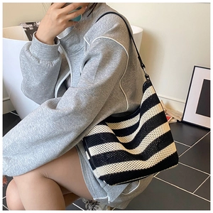 Detail view of a large woven striped tote bag worn by a model in a minimalist studio