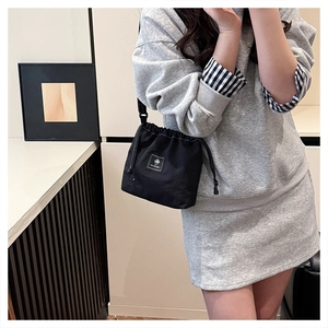 Black drawstring bucket bag made of washed fabric featuring white logo patch on a model