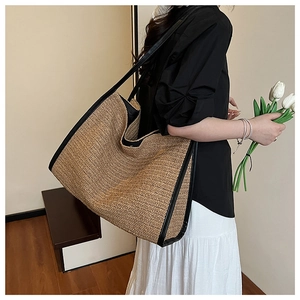 Macro detail of hand-woven straw tote bag with black leather straps on a model