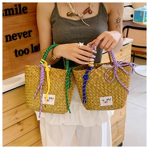 Detail of woven straw handbag featuring colorful braided rope handles and logo patch