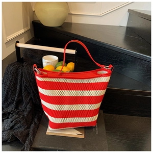 Close-up of red and white striped woven bucket bag with leather handles on a magazine