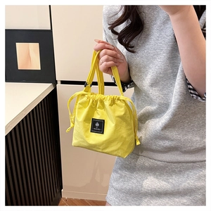 Detail of a bright yellow drawstring bucket bag with a minimalist black logo patch