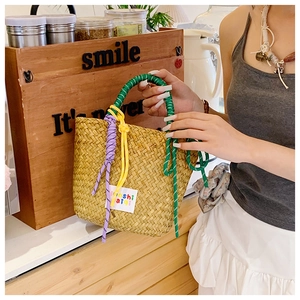 Detail of hand-woven straw tote bag with vibrant multicolored rope handles and a white tag