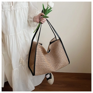 Detail of woven straw tote bag featuring herringbone texture and black leather handles