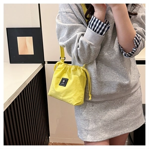 Close-up of lemon yellow drawstring canvas crossbody bag on a casual grey outfit