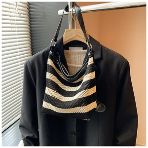 Detail of woven striped hobo bag featuring black leather straps and silver metal rings