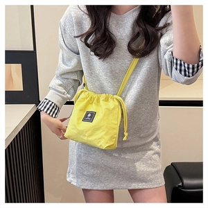 Detailed close-up of yellow drawstring crossbody bag with black square brand logo patch