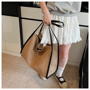 Detail of a large woven straw tote bag with black leather handles and chevron texture