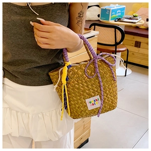 Detail of hand-woven straw tote bag with purple rope handle and yellow tassel accent
