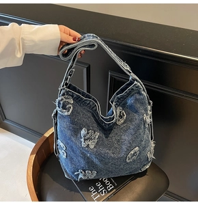 Detail of blue denim hobo bag featuring frayed letter patchwork and metallic hardware