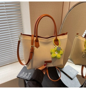 Détail d'un cabas en maille crème avec finitions en cuir marron et breloque fleurie