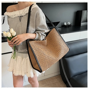 Close-up of woven straw tote bag with brown herringbone texture and black leather straps