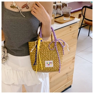 Close-up of woven straw handbag with purple and yellow braided rope handles and logo patch