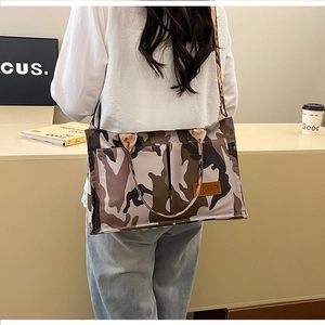 Detailed close-up of camouflage tote bag featuring a leather logo patch and wide strap