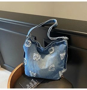 Close-up of blue denim tote bag featuring distressed white letter patches and soft fabric texture