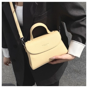 Détail du sac bandoulière crème en cuir grainé avec finitions argentées sur blazer noir