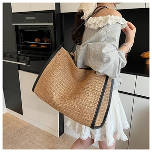 Close-up of woven straw tote bag with black leather straps in a cozy lifestyle setting