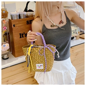 Detail of woven straw tote bag featuring colorful purple and yellow rope handles in a cafe