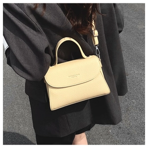 Détail d'un sac bandoulière jaune crème à texture litchi sur un costume gris foncé